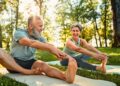 senior man and woman stretch their legs on yoga mats outside