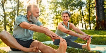 senior man and woman stretch their legs on yoga mats outside