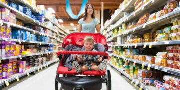A woman shops in a grocery store while pushing a stroller with a child