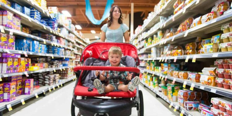A woman shops in a grocery store while pushing a stroller with a child