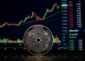 Cardano ADA coin stands in front of a trading screen showing a rising crypto price chart.