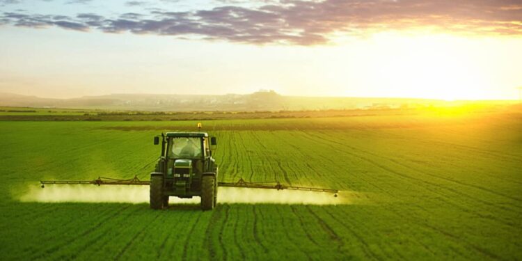 Tractor spraying a field of wheat with fertilizer