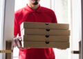 worker carries stack of pizza boxes for delivery
